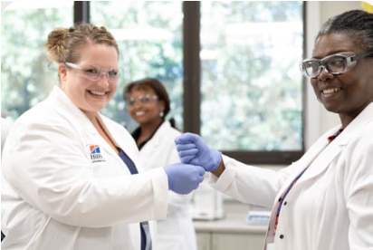 tres mujeres sonrientes, científicas con batas blancas y gafas protectoras