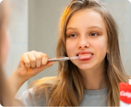 Niña cepillándose los dientes frente a un espejo como parte de una rutina de higiene bucal saludable.