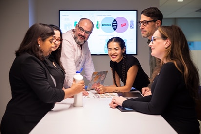 Seis empleados de Colgate-Palmolive en una sala de reuniones analizando un concepto de producto, con una diapositiva de presentación en una pantalla detrás de ellos.